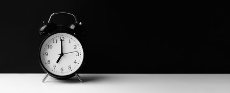 Black alarm clock on white table on black background.の写真素材