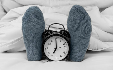 Alarm clock on bed next to female feet in socksの写真素材