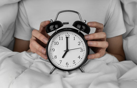 Woman's hand holding black alarm clock in the bedの写真素材