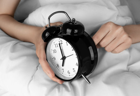 Woman's hand Starts up black alarm clock in her bedの写真素材