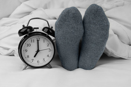 Alarm clock on bed next to female feet in socksの写真素材