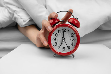 Woman's hand turning off red alarm clock on night tableの写真素材