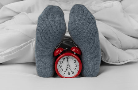 Alarm clock on bed next to female feet in socksの写真素材