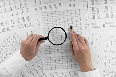 Woman holding a magnifying glass pointing at numbers on financial documents. ?oncept of finance, search and accounting.の写真素材