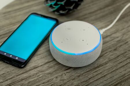 Voice controlled speaker with activated voice recognition, on wood background near blue phoneの写真素材