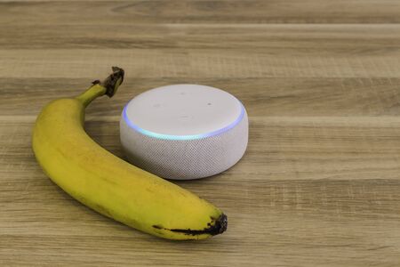 Voice controlled speaker with activated voice recognition, on wood background with bananaの写真素材