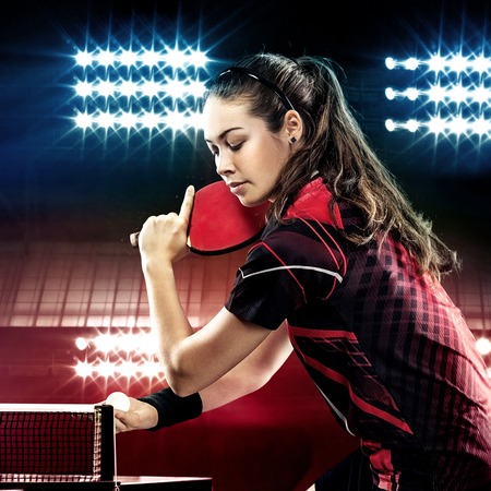 Young pretty sporty girl playing table tennis on black background with lightsの写真素材