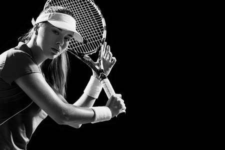 Portrait of beautiful girl tennis player with a racket isolated on black backgroundの写真素材