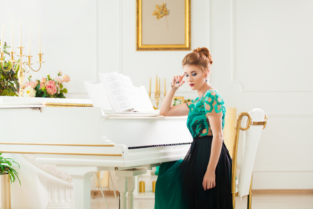 Fashion young pretty redhead lady playing grand pianoの写真素材