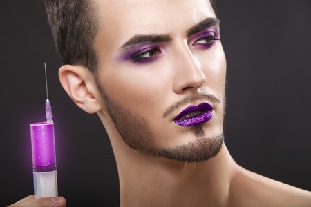 Pretty sensual gay man with art makeup and beard. Color syringe in the hand.の写真素材