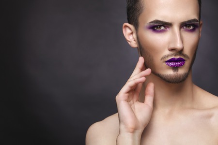 Pretty sensual gay man with art makeup and beard. Color syringe in the hand.