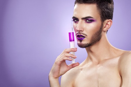 Pretty sensual gay man with art makeup and beard. Color syringe in the hand.の写真素材