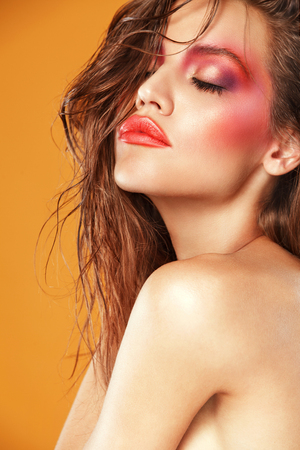 Sexy brunette woman with art makeup and wet hair beauty on orange backgroundの写真素材