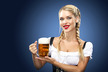 Half-length portrait of young sexy blonde with big breast wearing black dirndl with white blouse holding the beer mug Isolated on dark backgroundの写真素材