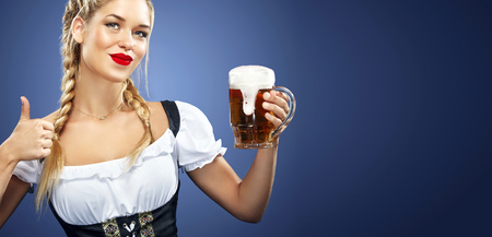 Half-length portrait of young sexy blonde with big breast wearing black dirndl with white blouse holding the beer mug Isolated on dark backgroundの写真素材
