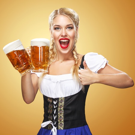 Half-length portrait of young sexy blonde with big breast wearing black dirndl with white blouse holding the beer mug Isolated on dark backgroundの写真素材