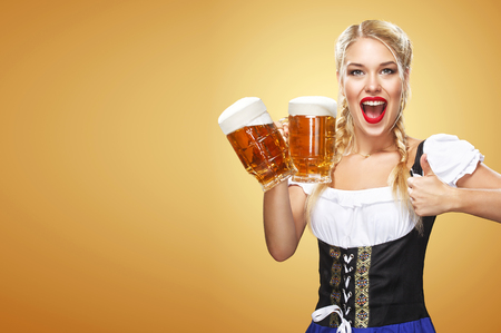 Half-length portrait of young sexy blonde with big breast wearing black dirndl with white blouse holding the beer mug Isolated on dark backgroundの写真素材
