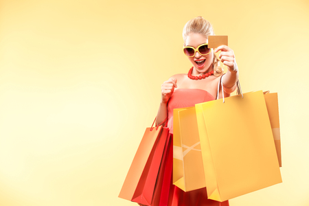 Happy young woman shopping in black friday holiday. Girl with many color bags on yellow background.の写真素材