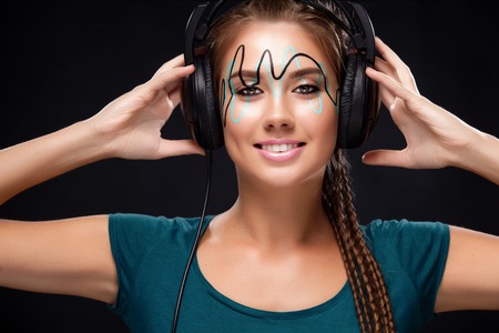 Modern young woman with art makeup enjoys listening to music in headphones. Positive emotions, leisure. Copy space.の写真素材