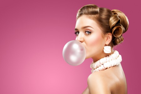 Beautiful blonde woman blowing pink bubble gum. Fashion portrait.の写真素材