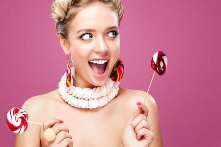 Attractive woman with lollipop in hand on pink backgroundの写真素材