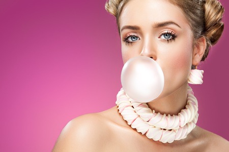 Beautiful blonde woman blowing pink bubble gum. Fashion portrait.の写真素材