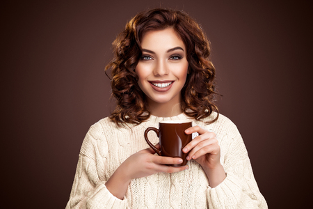 beautiful smiling woman with a cup of tea on the brown background. Coffee advertisement, copy space.の写真素材