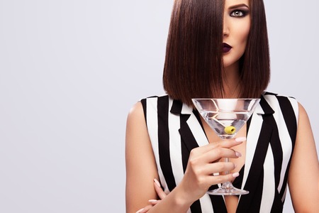 Fashion studio photo of beautiful young lady with martini glass. Perfect face makeup. Beauty makeup.の写真素材