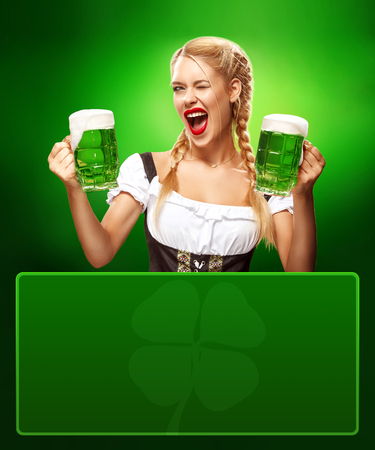 St Patricks Day. Young sexy Oktoberfest waitress, wearing a traditional Bavarian dress, serving big beer mugs on blue background with copy spaceの写真素材