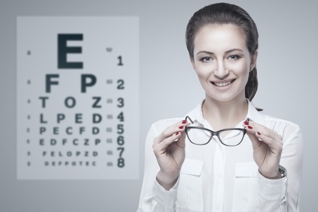 Woman holding glasses in hands with Snellen test chart on background.の写真素材