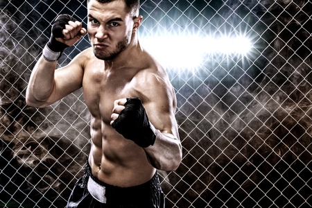 Sportsman muay thai boxer fighting in boxing cage. Background with lights and smoke. Copy Space. Sport concept.の写真素材