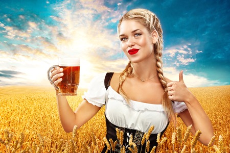 Half-length portrait of young sexy blonde with big breast wearing black dirndl with white blouse holding the beer mug Isolated on dark backgroundの写真素材