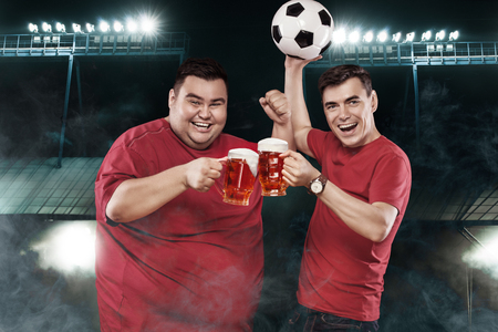 Half-length portrait of young men with holding the beer mugs at the stadium and watching soccer matchの写真素材