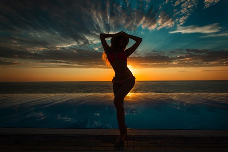 Summer Vacation. Silhouette of beauty dancing woman on sunset near the pool with ocean view.の写真素材