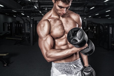 Athletic shirtless young sports man - fitness model holds the dumbbell in gym. Copy space fore your text.の写真素材