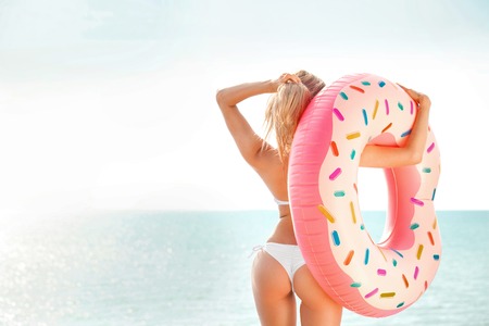 Summer Vacation. Enjoying suntan woman in white bikini with donut mattress near the sea.の写真素材