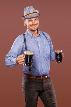 Portrait of Oktoberfest man in hat, wearing a traditional Bavarian clothes, serving big beer mugs.の写真素材