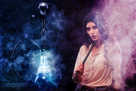 Young, beautiful woman in the night club or bar smoke a hookah. The pleasure of smoking. Sexy smoke.の写真素材