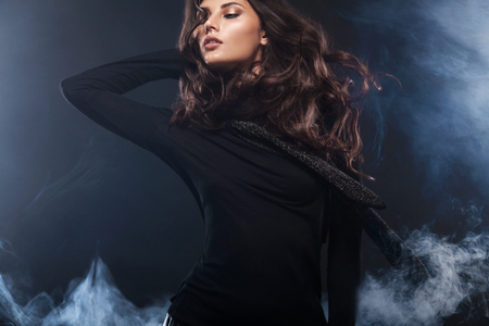 Fashion photo of a beautiful young woman in a pretty dress posing over black background with smoke. Fashion photo with copy spaceの写真素材
