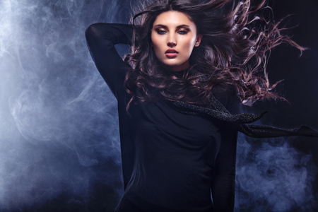 Fashion photo of a beautiful young woman in a pretty dress posing over black background with smoke. Fashion photo with copy spaceの写真素材