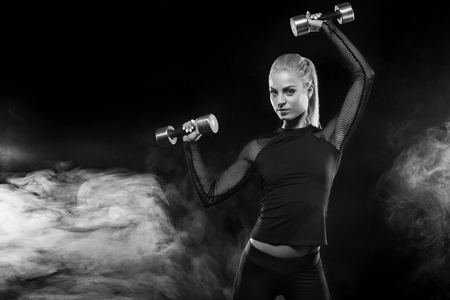 Sporty beautiful woman with dumbbells makes fitness exercising at black background to stay fitの写真素材