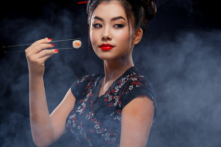 Asian woman with sushi eating sushi and rolls on a black background. Black Friday sushi sale.の写真素材