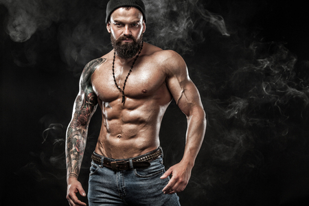 Handsome fit man posing wearing in jeans with tattoo. Sport and fashion concept isolated on black background.の写真素材