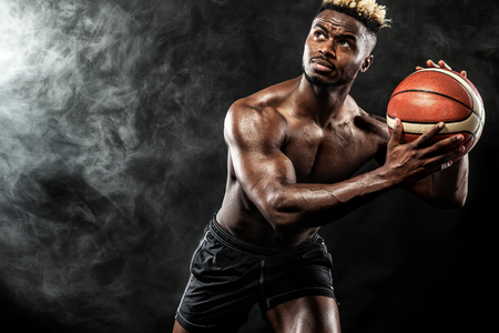 Portrait of male basketball player with a ball over black background. Fit young man in sportswear holding basketball.の写真素材