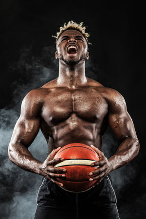 Portrait of afro-american sportsman, basketball player with a ball over black background. Fit young man in sportswear holding ball.の写真素材