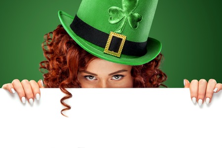 St Patricks Day. Young sexy ginger Oktoberfest waitress, wearing a traditional Bavarian dress, serving big beer mugs on green background with banner for copy spaceの写真素材