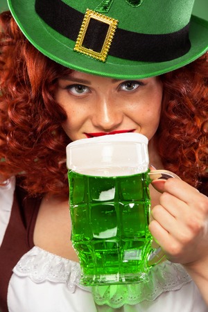 St Patrick Day. Young redhead Oktoberfest waitress, wearing a traditional Bavarian dress, serving big beer mugs on green background with copy spaceの写真素材