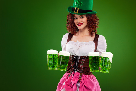 St Patricks Day. Young sexy Oktober fest waitress, wearing a traditional Bavarian dress, serving big beer mugs on green background with copy spaceの写真素材