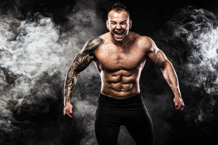 Handsome fit man posing wearing in jeans with tattoo. Sport and fashion concept isolated on black background.の写真素材