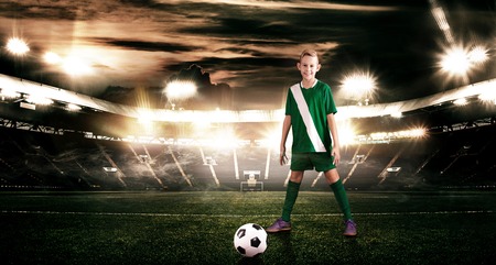 Kid - soccer player. Boy forward in football sportswear on stadium with ball. Sport concept.の写真素材